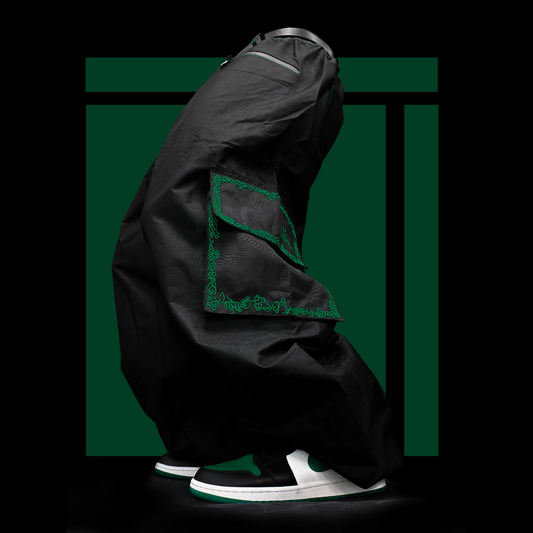 a pair of baggy snowpants (ski pants or snowboad pants) stand in front of a green square. they do not have a torsoe, but appear to be lifelike. the pants are black, with colorful embroidery around the pockets. green embroidery.