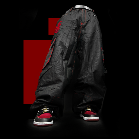 Baggy black snowpants with vibrant red accents, ideal for snowboarding and skiing. These durable, waterproof pants feature a unique green embroidery design on the pocket, showcasing a stylish look for both ski and snowboard enthusiasts. Perfectly crafted to combine fashion and function, these baggy ski pants ensure comfort and mobility on the slopes.